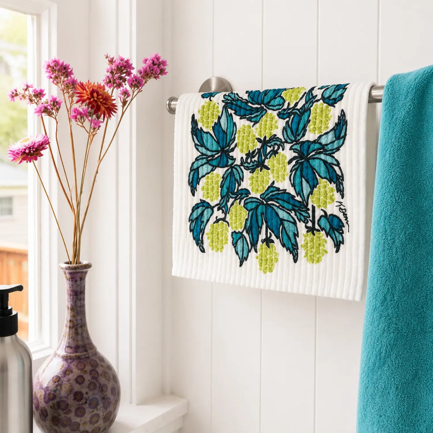 Hops Swedish dishcloth hanging beside a teal towel in a bright kitchen