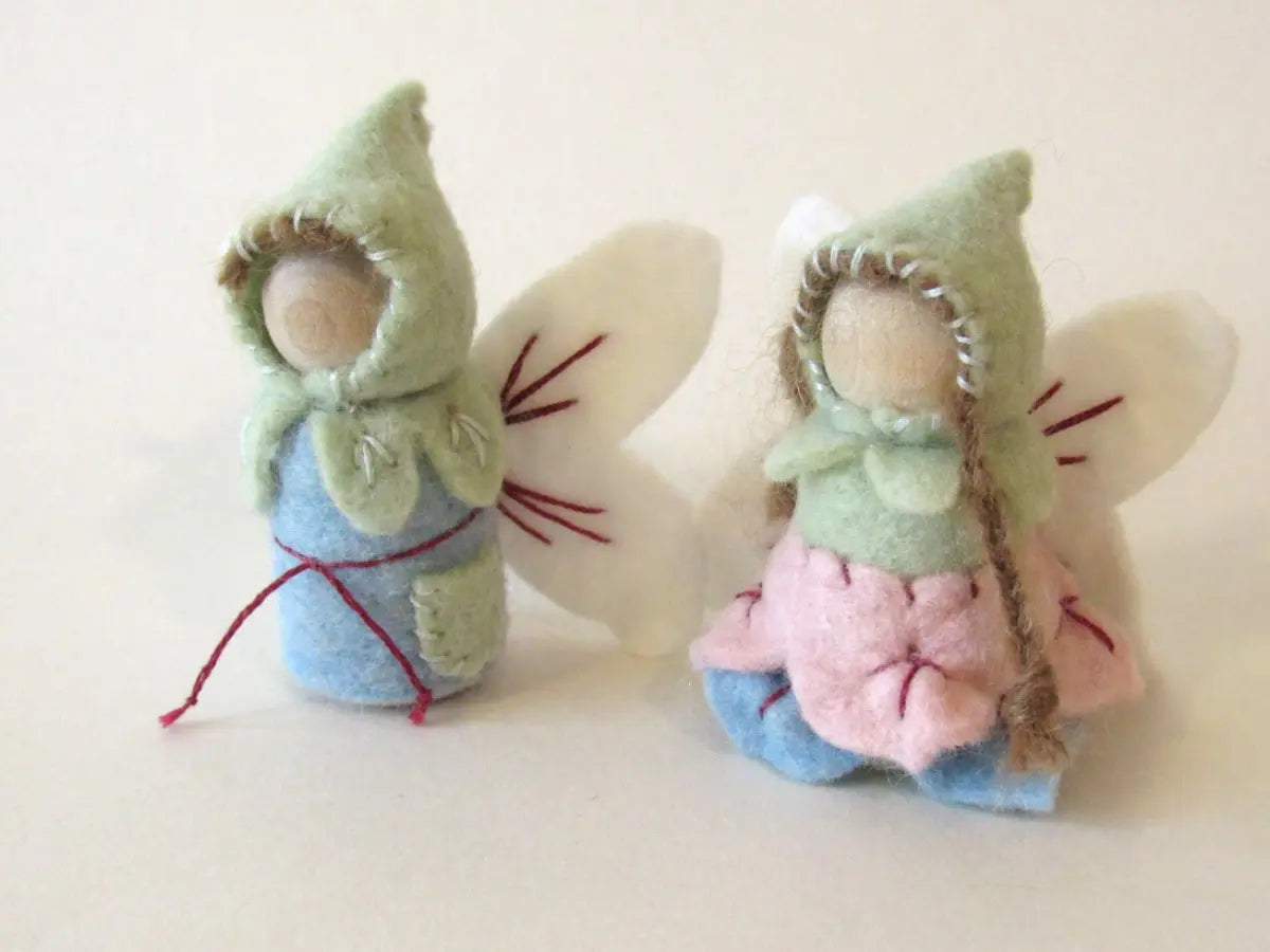 Two small fairy wool dolls with green hats and colorful dresses on a white background