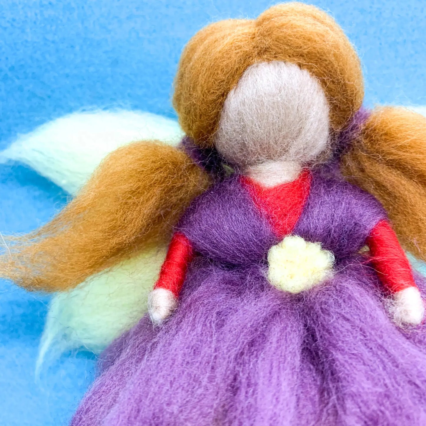 Felted fairy doll with brown hair, purple dress, and red shirt on a blue background