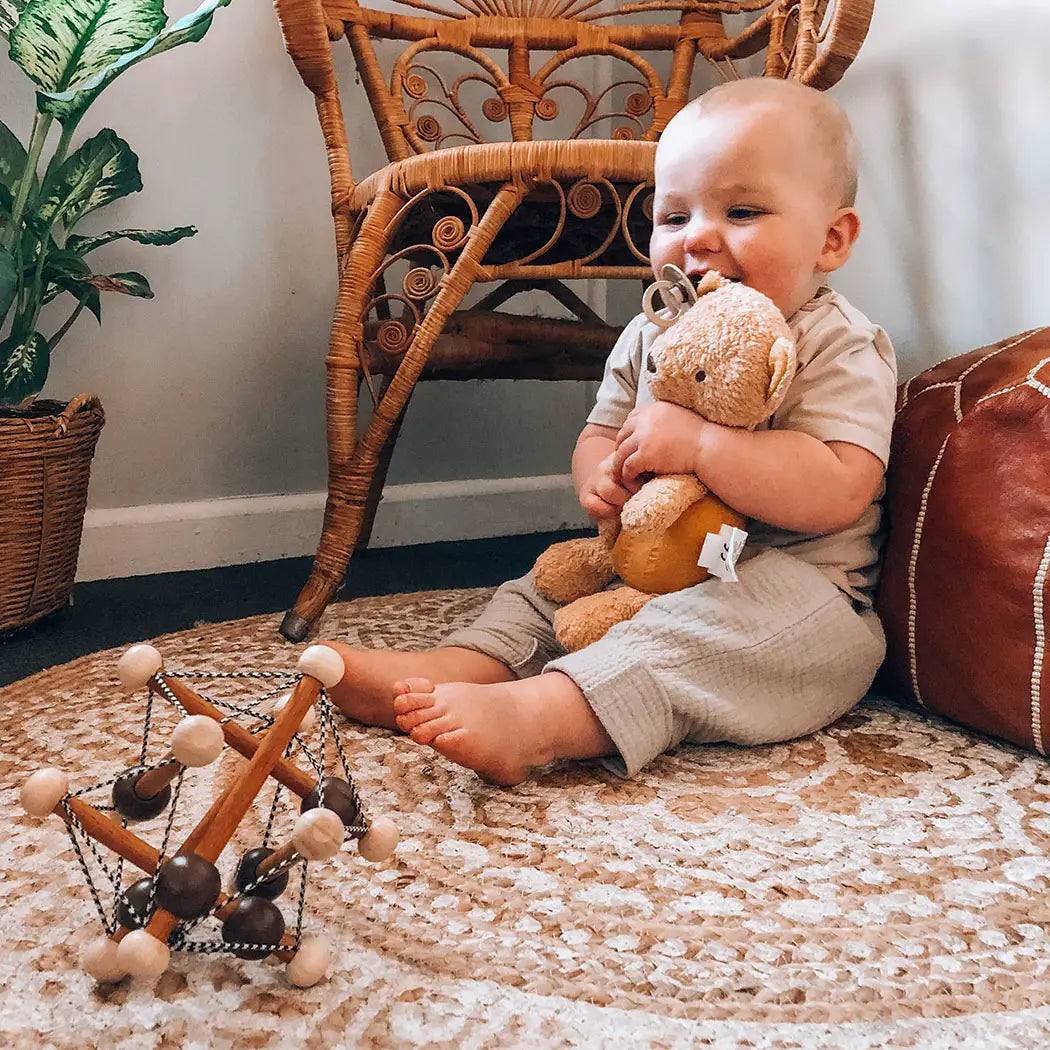 Toddler holding organic teddy bear sitting on floor