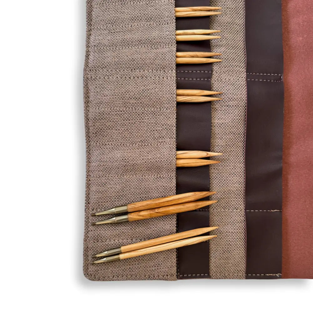 Set of wooden knitting needles in a brown fabric case on a white background