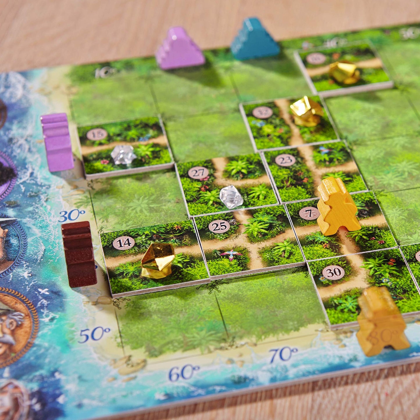 Board game with green tiles and player pieces on a wooden surface