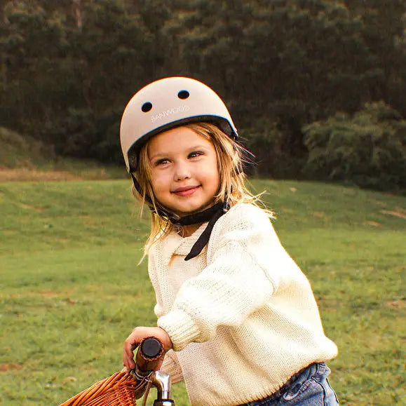 Child wearing a beige bike helmet and holding a bike in a grassy field