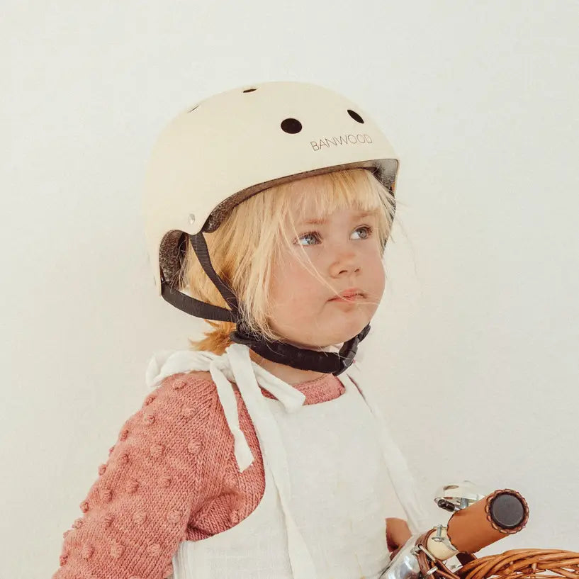 Child wearing a creme helmet with 'Banywood' branding, holding a toy bike.