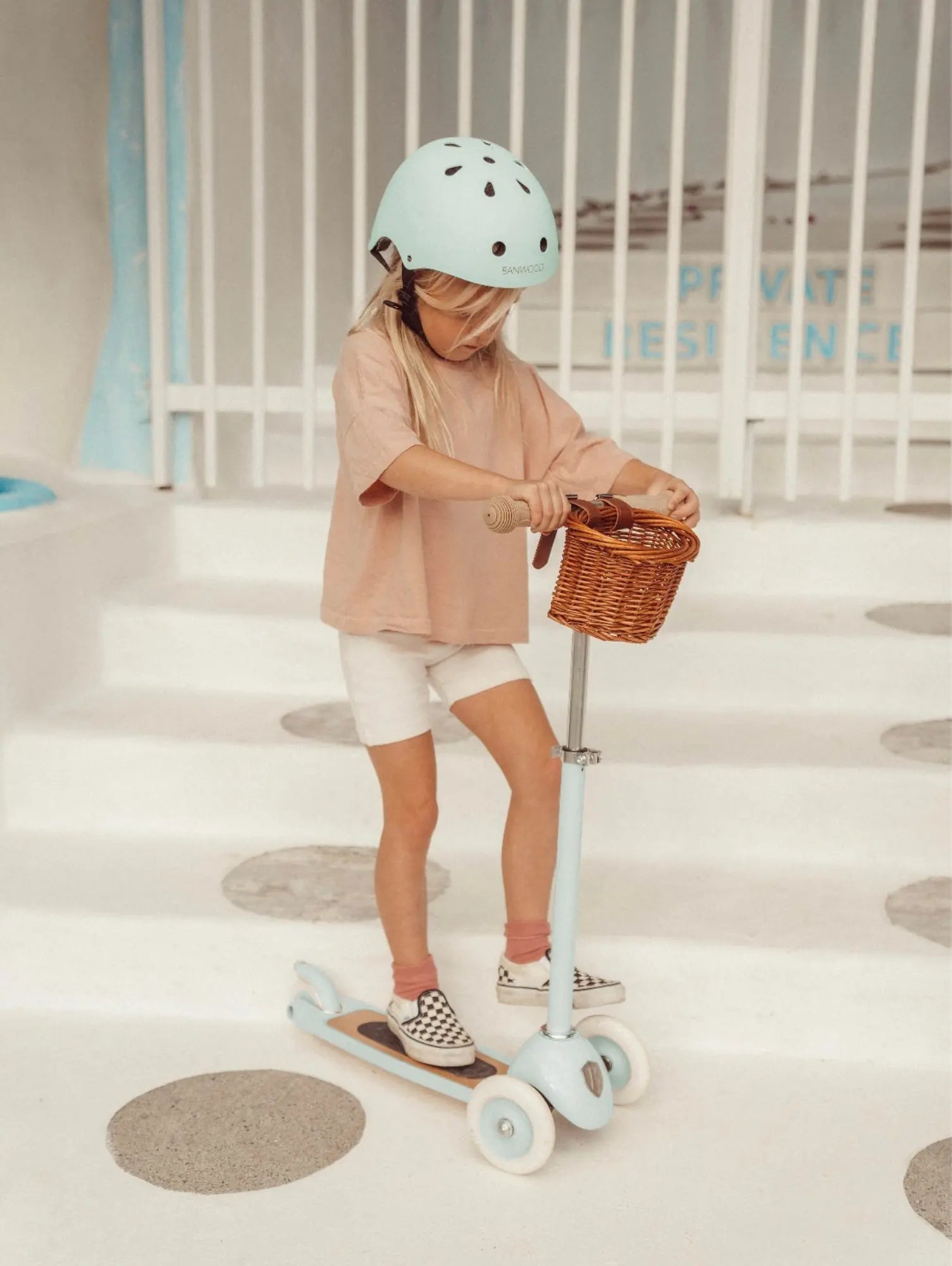 Child wearing a helmet and riding a scooter with a basket indoors.