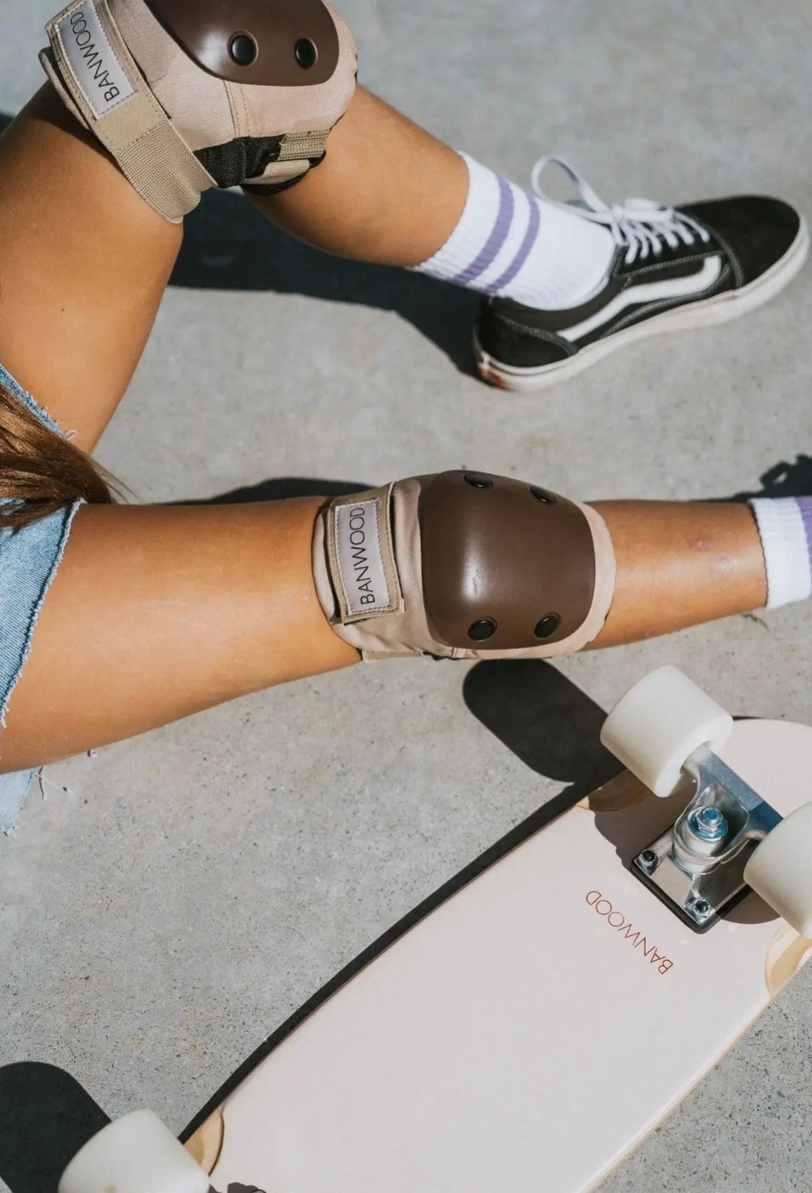 Person wearing knee pads and sitting next to a skateboard with visible brand logos.