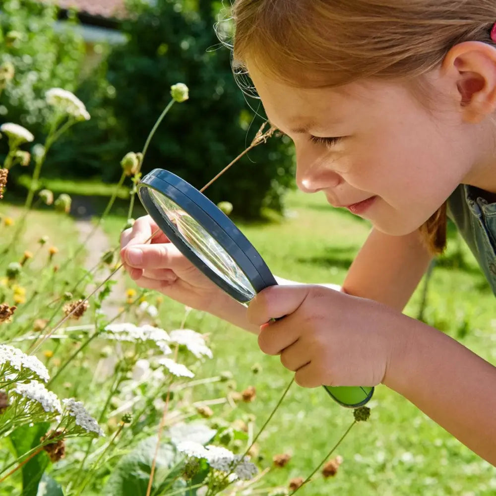 Child examining flowers through a magnifying glass in a garden