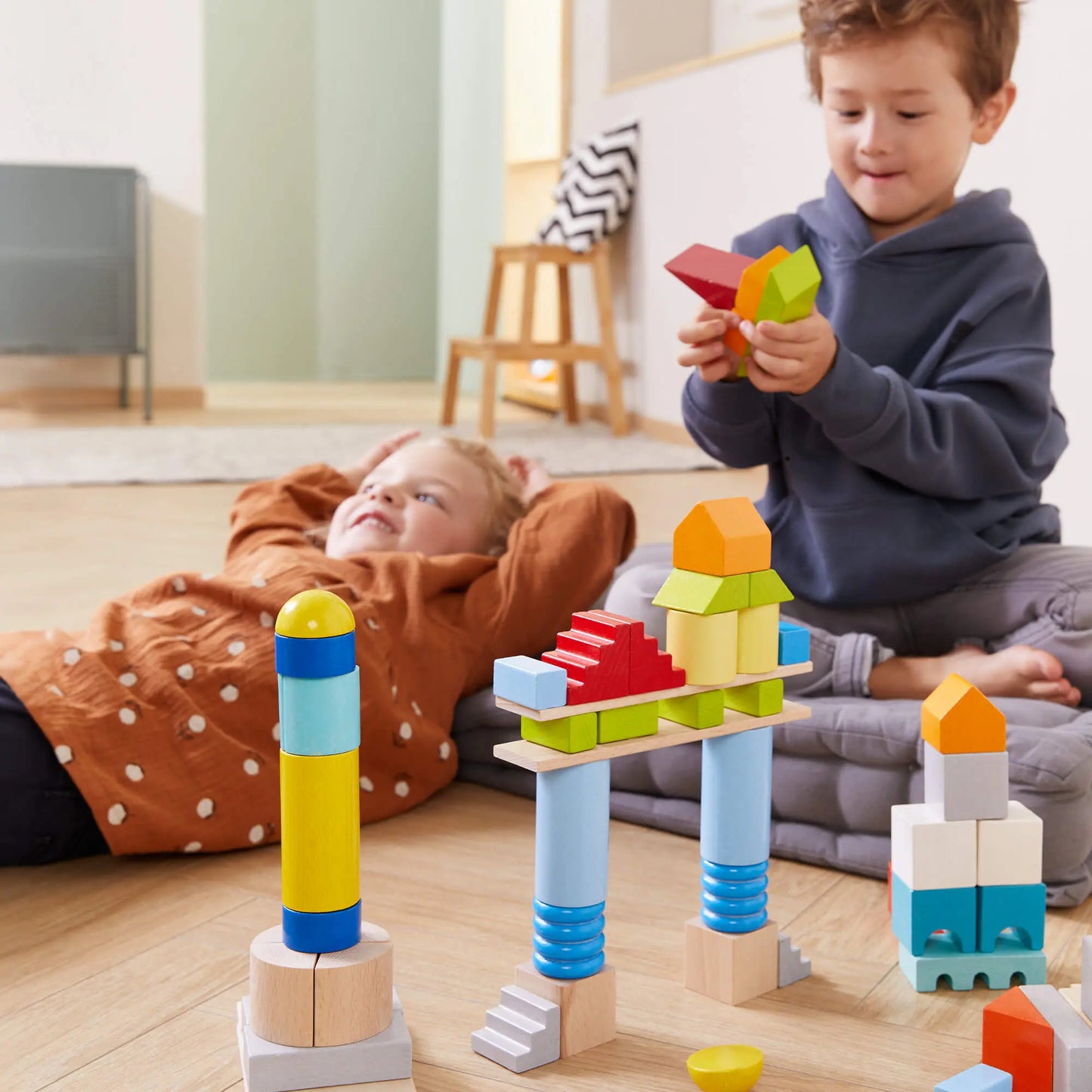 Two children playing with colorful building blocks on a wooden floor.