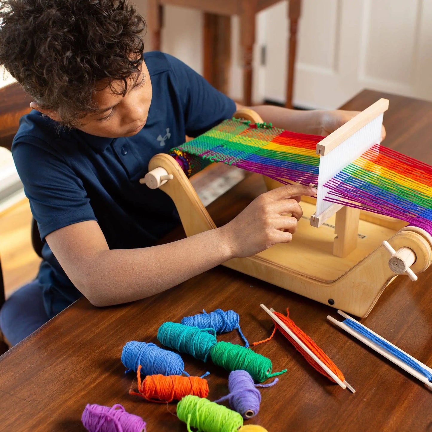 Child weaving on a beginner wooden table loom with rainbow yarn