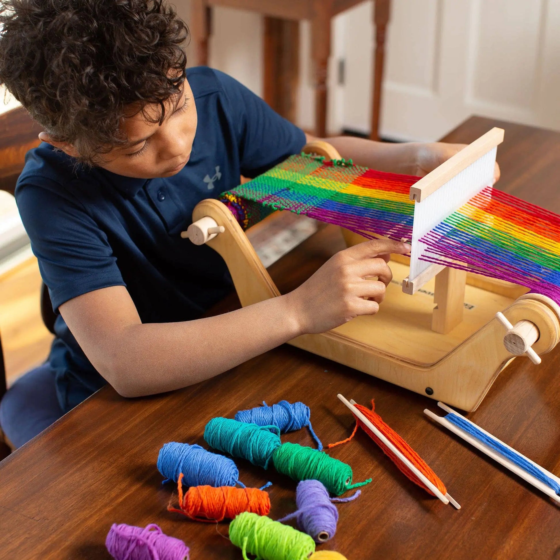 Child weaving on a beginner wooden table loom with rainbow yarn