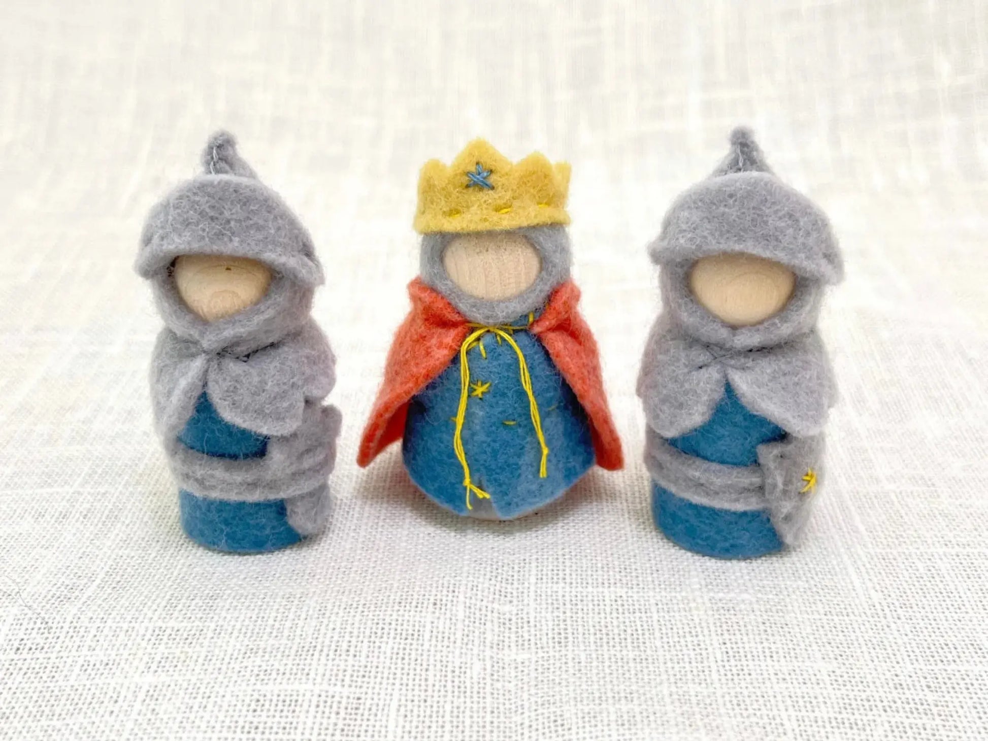 Three felted dolls dressed as a king and two knights on a textured white background