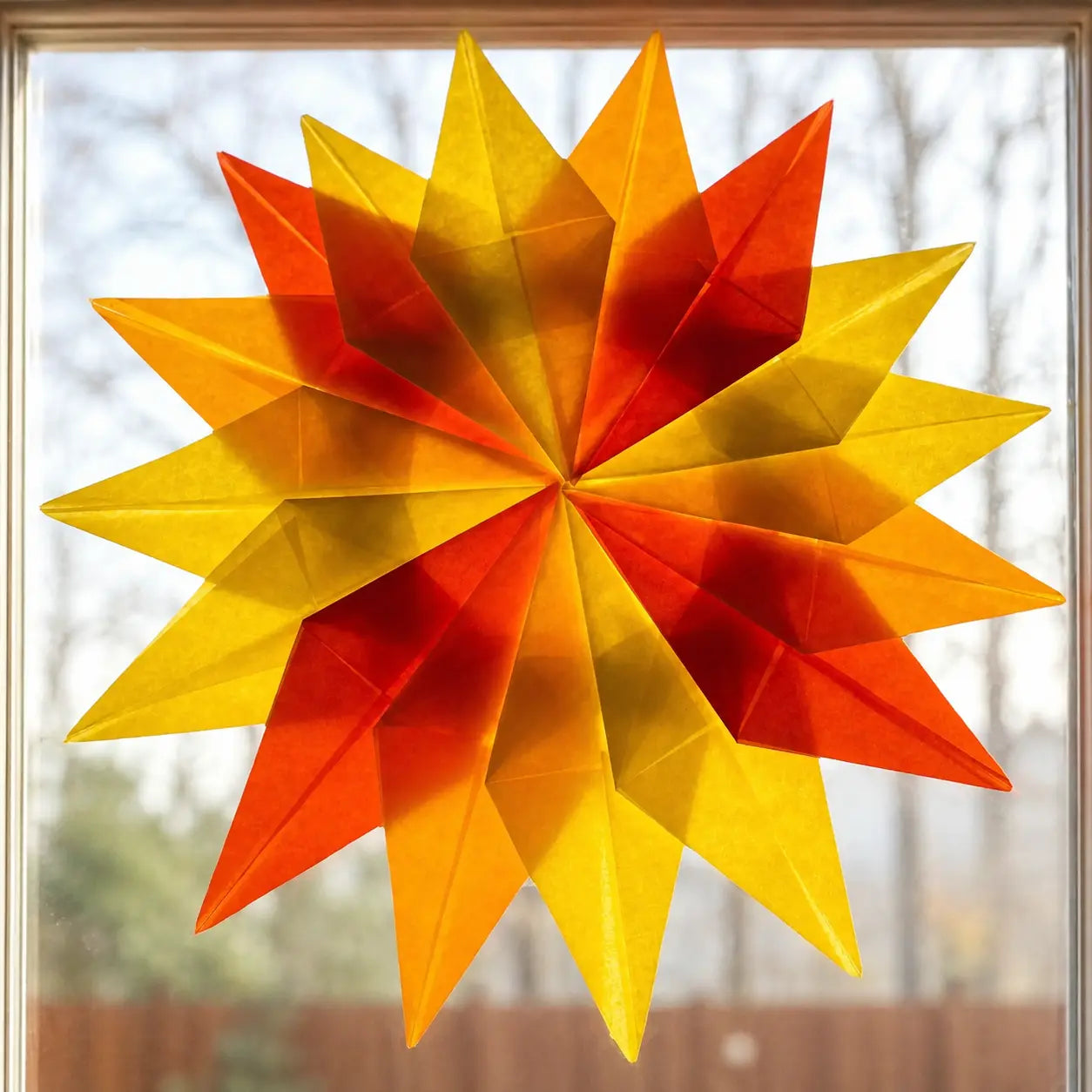 A handmade Waldorf window star with a layered, geometric design in vibrant shades of yellow, orange, and red