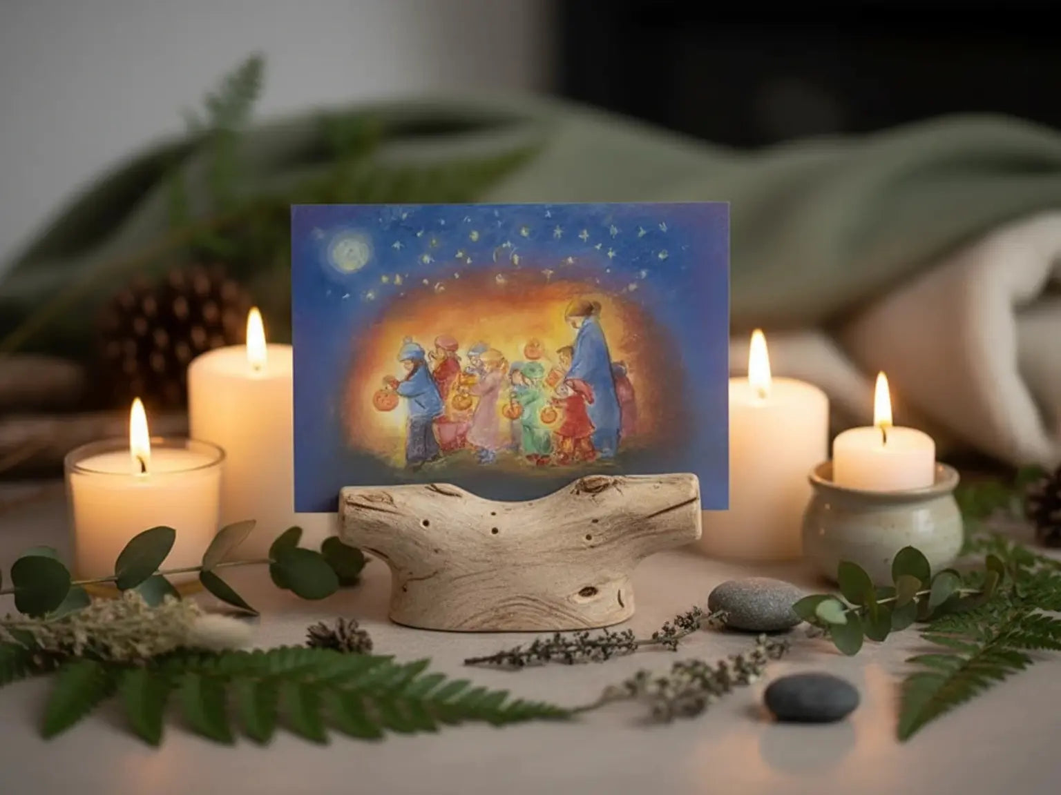 Festive card with Martinmas lantern procession scene surrounded by candles and greenery on a table.