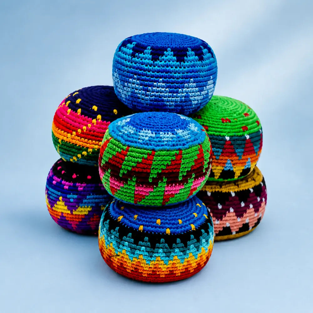 Stack of colorful woven cotton toss balls in hacky sack style on a light blue background