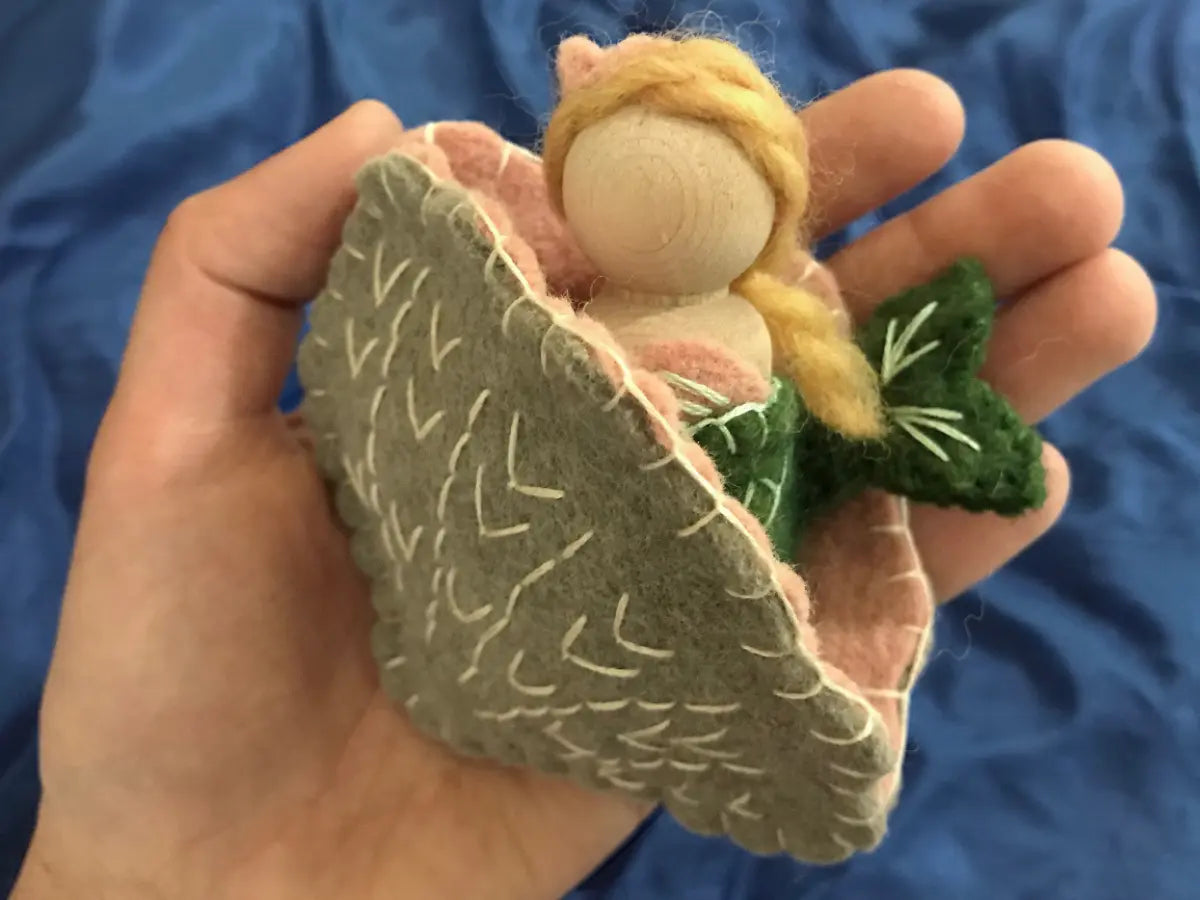 Hand holding a small mermaid peg doll with shell against a blue background