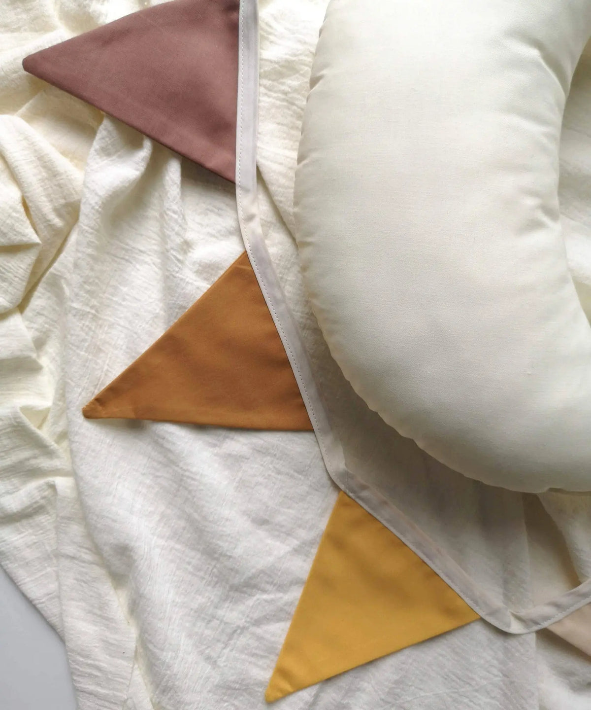 Soft linen pennant garland styled with neutral textiles and a cushion for a warm children’s room or playroom.