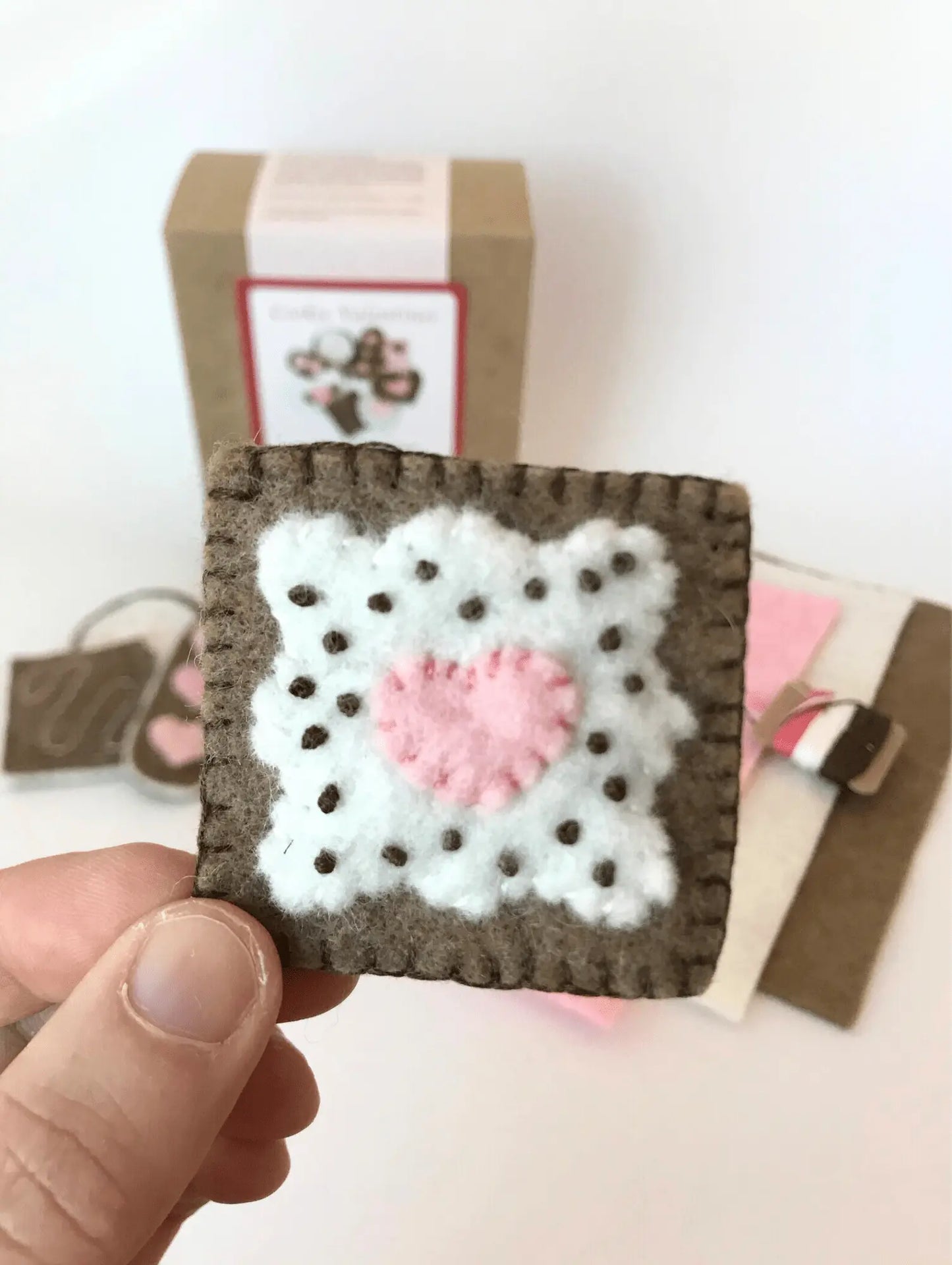 Handmade crochet square with a pink heart held by a hand against a neutral background