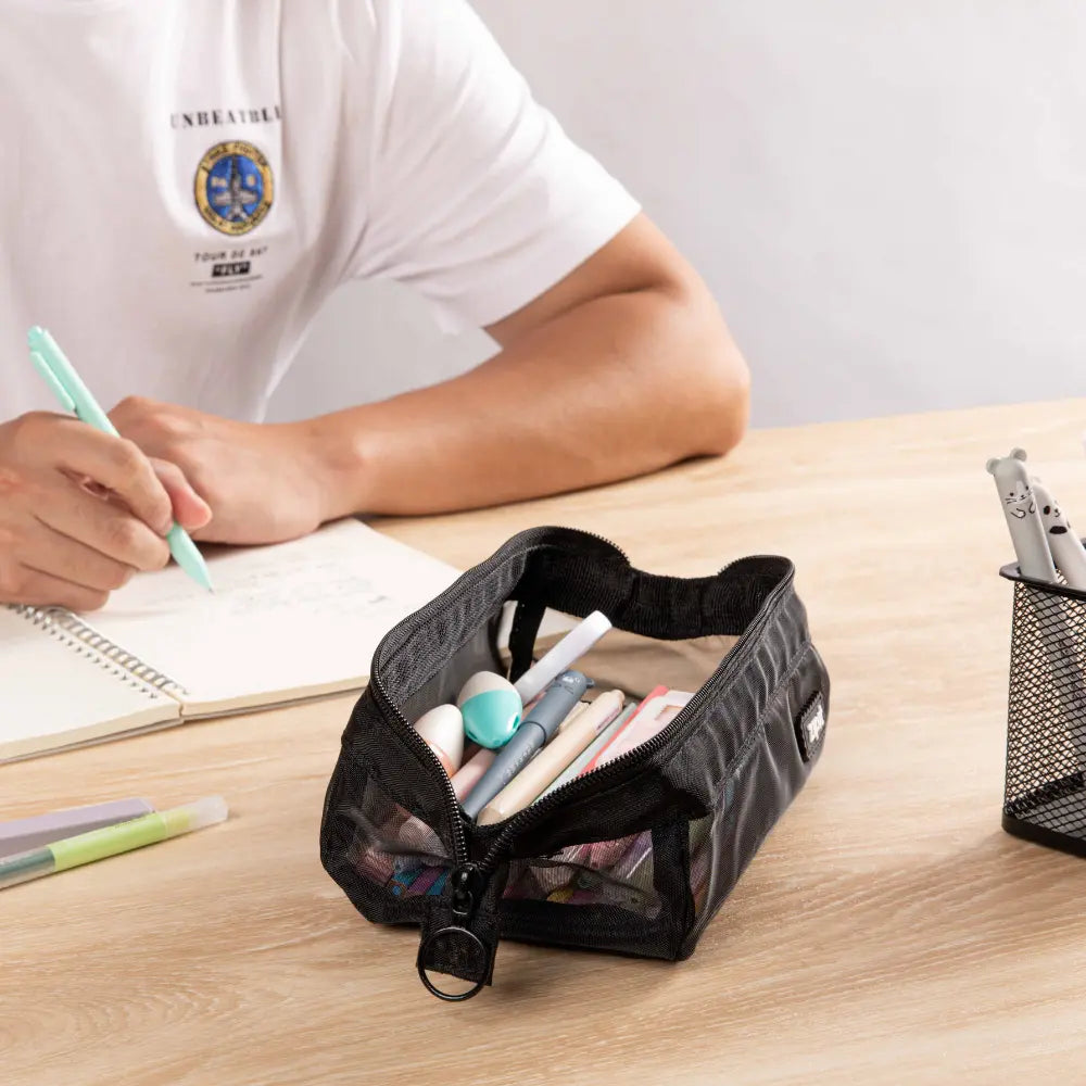 Black mesh pencil case on a desk with pencils and small school supplies for writing practice