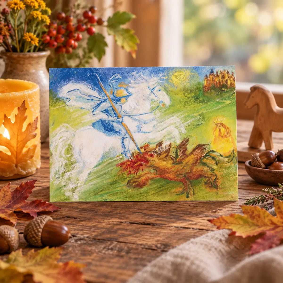 Michaelmas postcard with Saint George and the dragon displayed on an autumn seasonal table with beeswax candle, leaves, and acorns