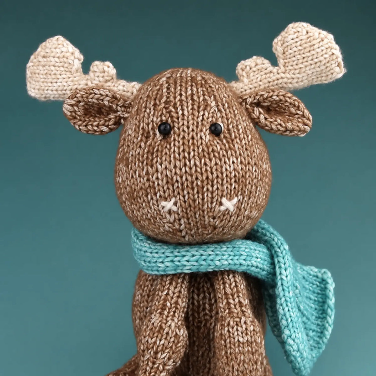 Finished Maddie Moose hand-knit toy seated with cream hooves, antlers, and blue scarf