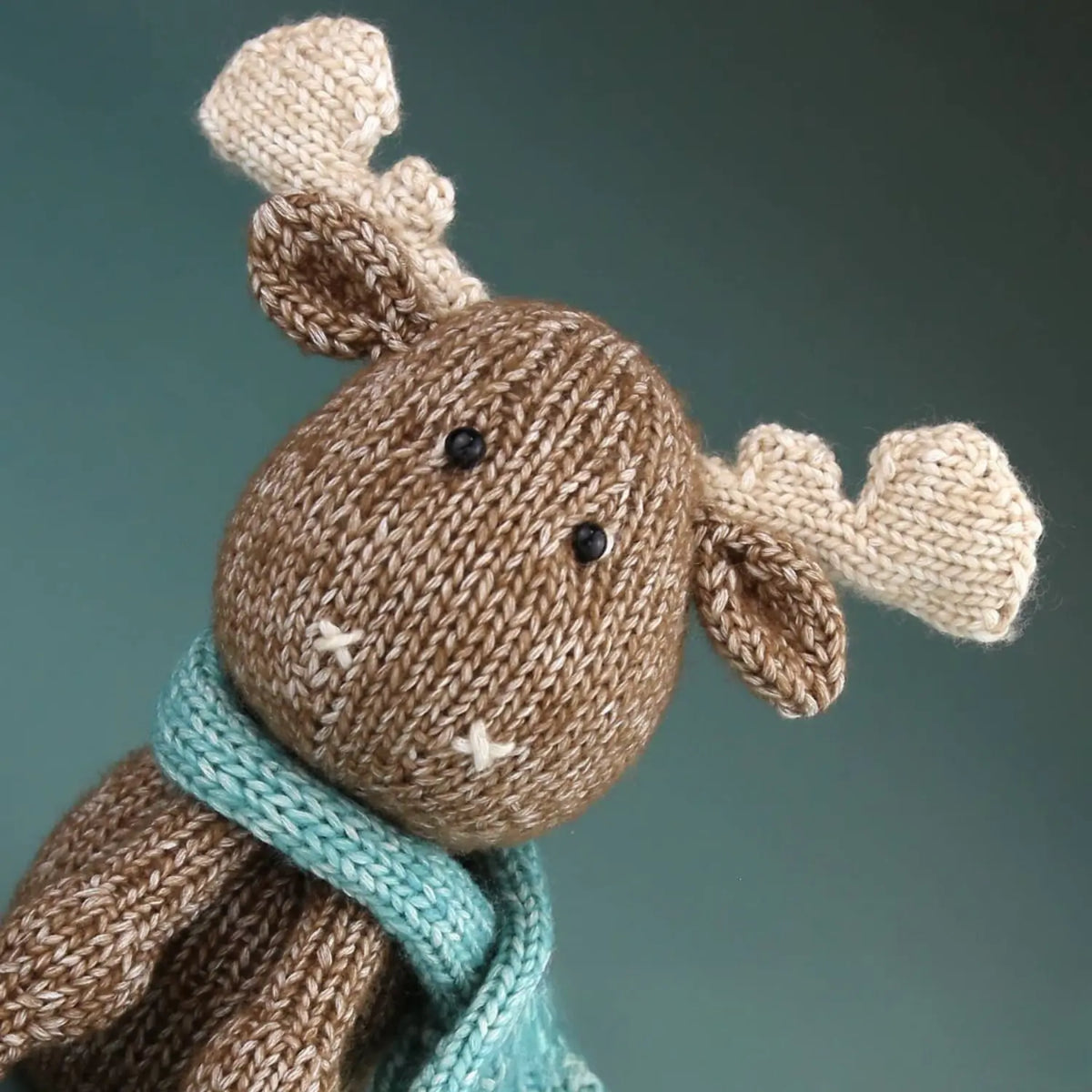 Close-up of Maddie Moose showing knitted antlers, safety eyes, and blue scarf