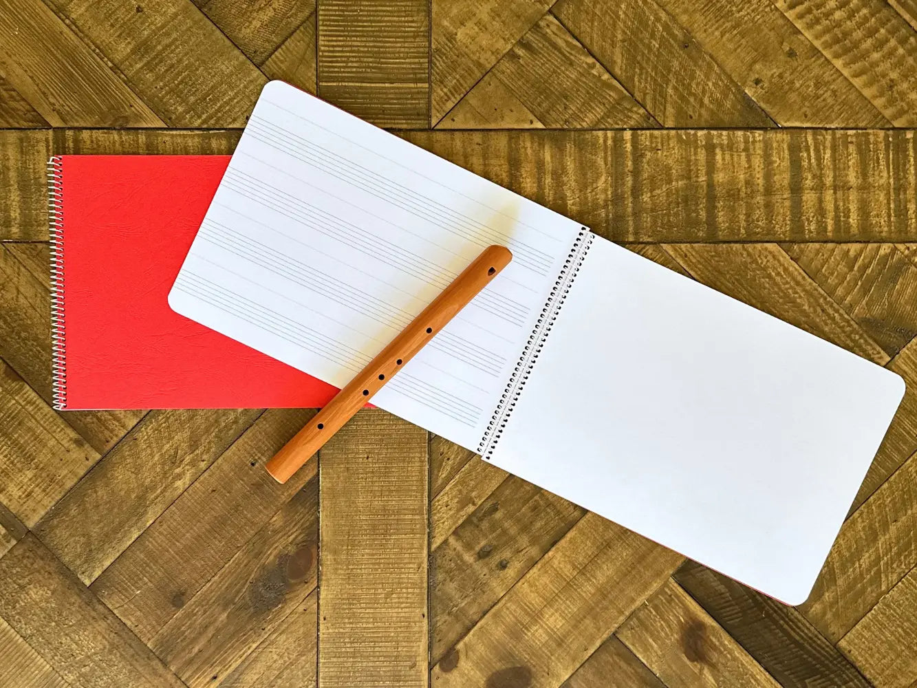 Open music notebook with wooden flute on a wooden surface