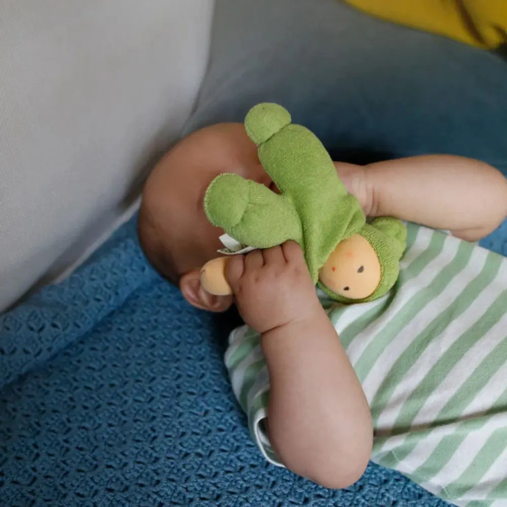 Baby holding a green Nanchen Waldorf doll with painted face with a striped outfit