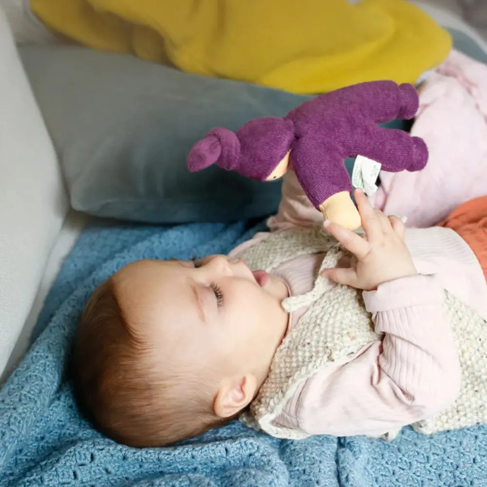 Baby playing with a purple Nanchen first doll on a blue blanket