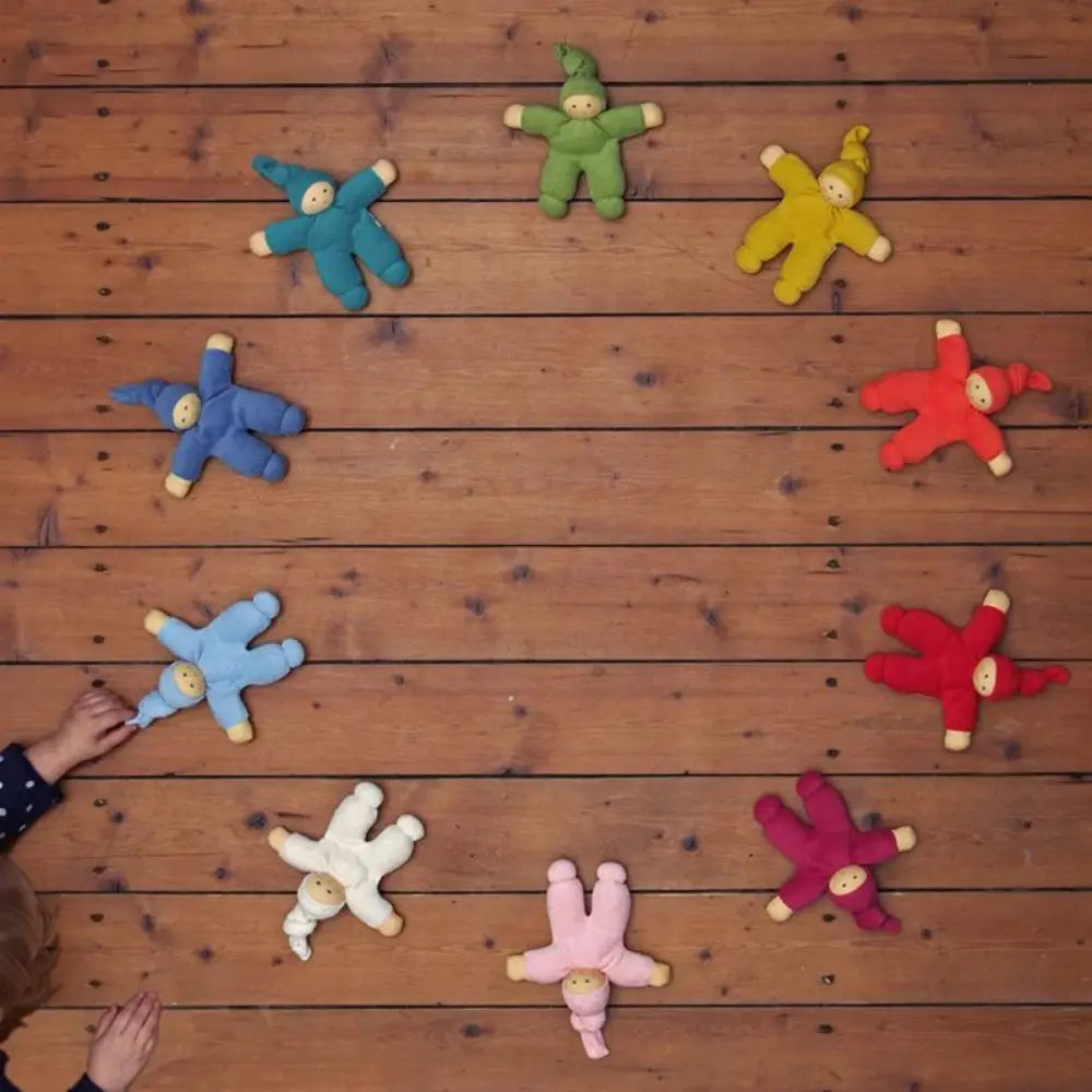 Colorful plush Waldorf dolls arranged in a circle on a wooden floor.