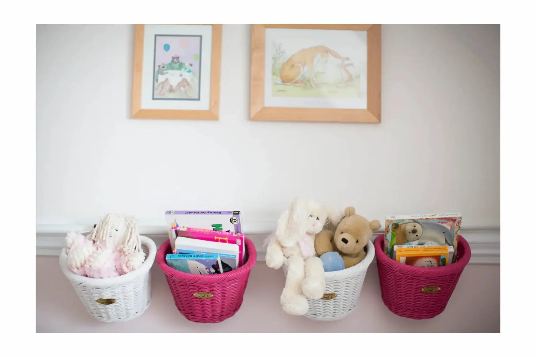 Four baskets containing toys and books on a shelf with framed pictures on the wall.