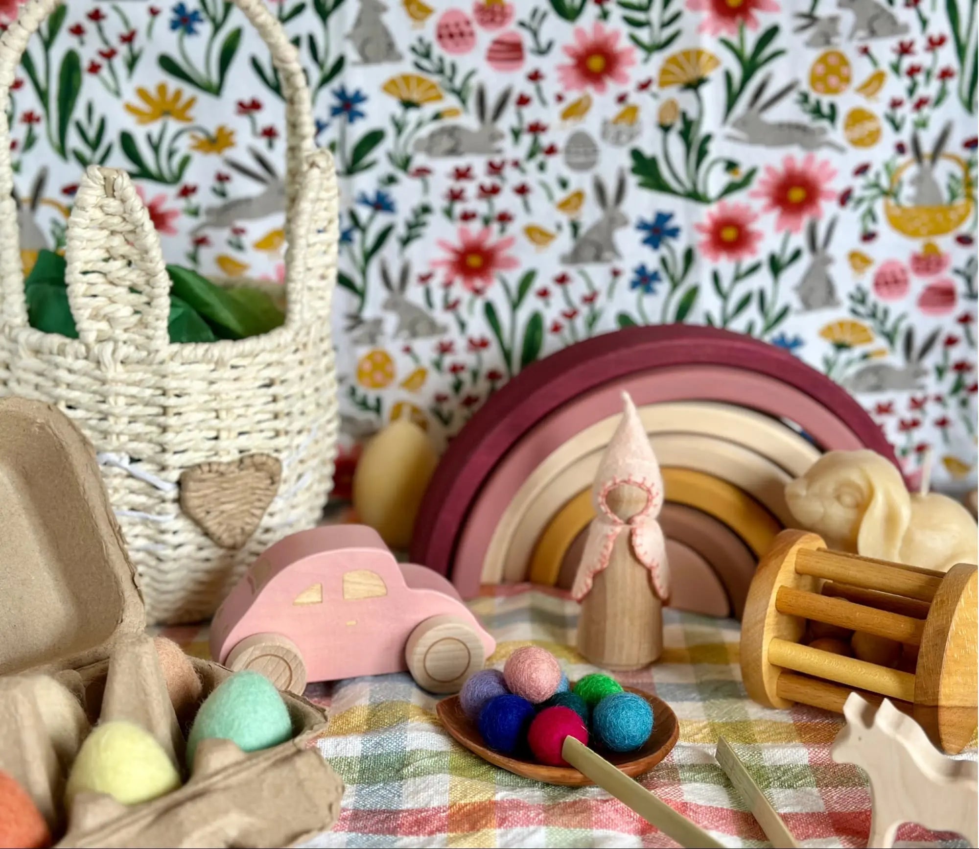 Colorful wooden Easter toys on a checkered tablecloth with a floral-patterned wall in the background