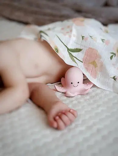 Baby lying under muslin blanket next to natural rubber octopus toy during early sensory play