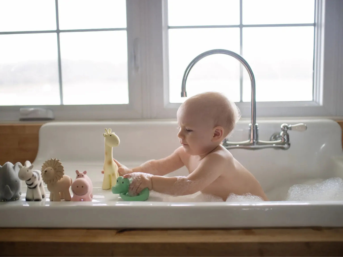 Baby playing in bath with natural rubber safari animal toys including giraffe during water play