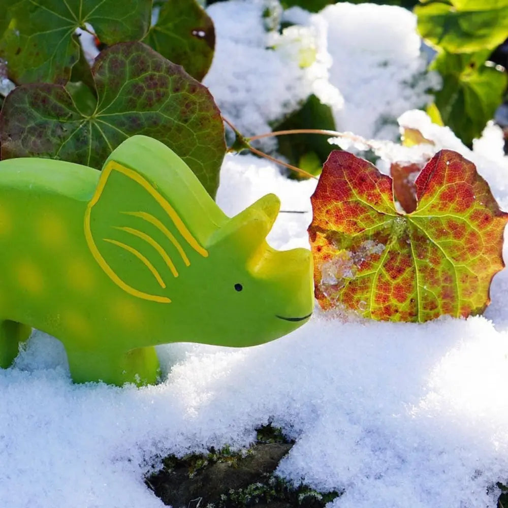 Natural rubber triceratops dinosaur toy outdoors in snow with plants for imaginative toddler play