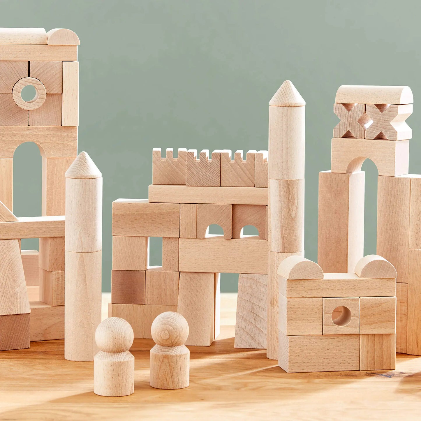 Natural wooden building blocks for open ended play on a wooden surface with a light green background