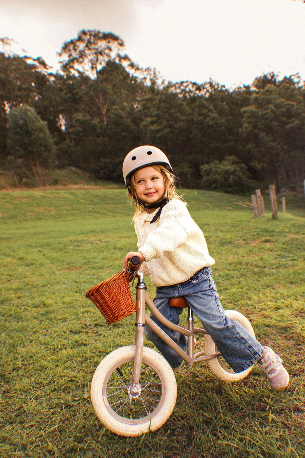 Child riding a balance bike in a grassy field with trees in the background
