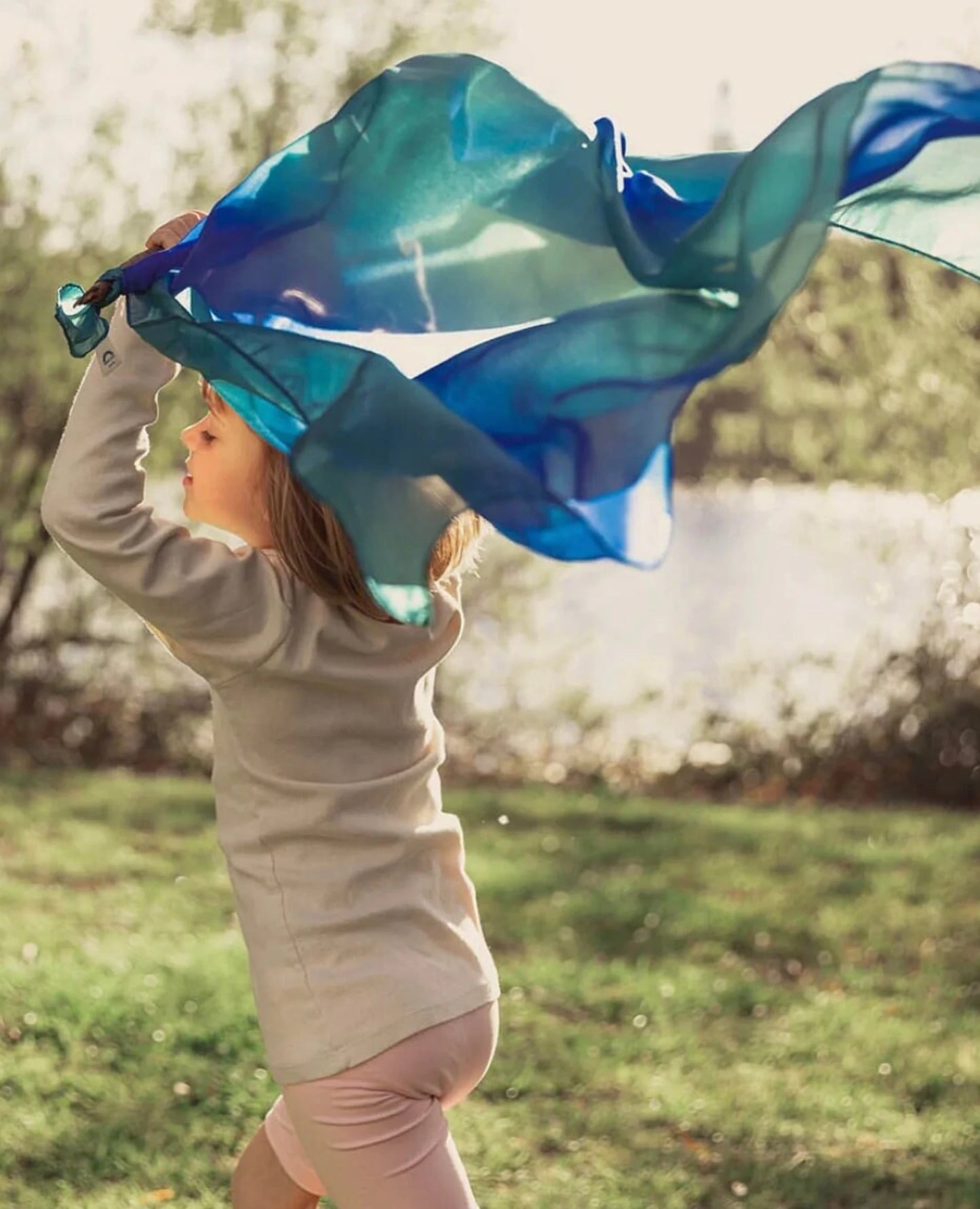 Earth playsilk in ocean held by a running girl in a grassy yard