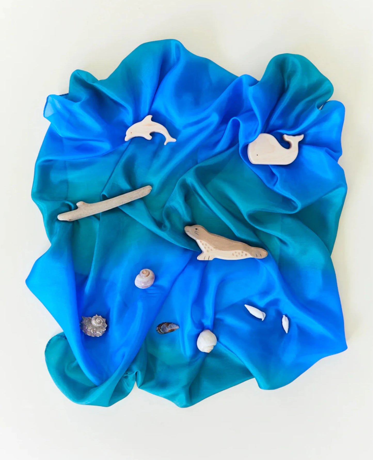 Earth playsilk in ocean with wooden toys on top on a light background