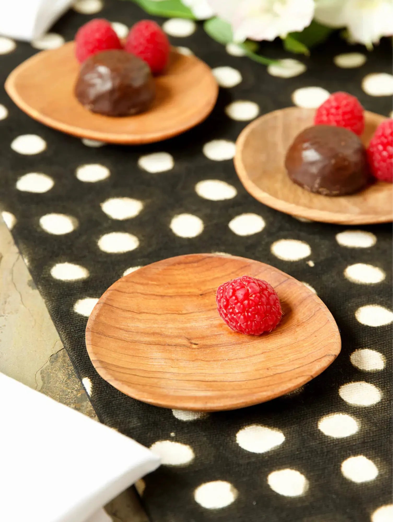 Wooden plates with chocolate truffles and raspberries on a black and white polka dot surface.