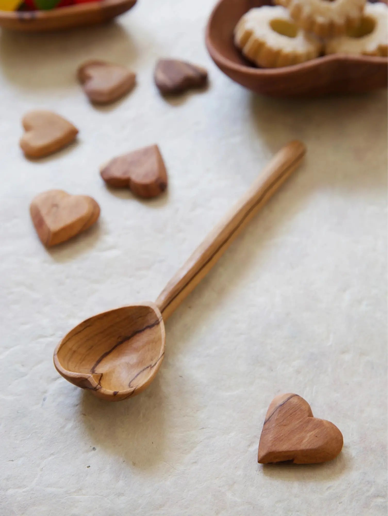 Hand-carved olive wood heart spoon on kitchen countertop with wooden hearts and cookies in background showing everyday use