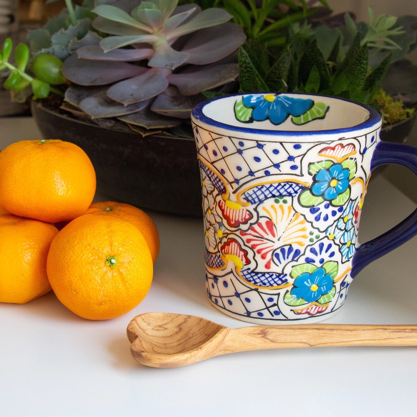 Hand-carved olive wood heart spoon shown with coffee cup and tangerines for size comparison