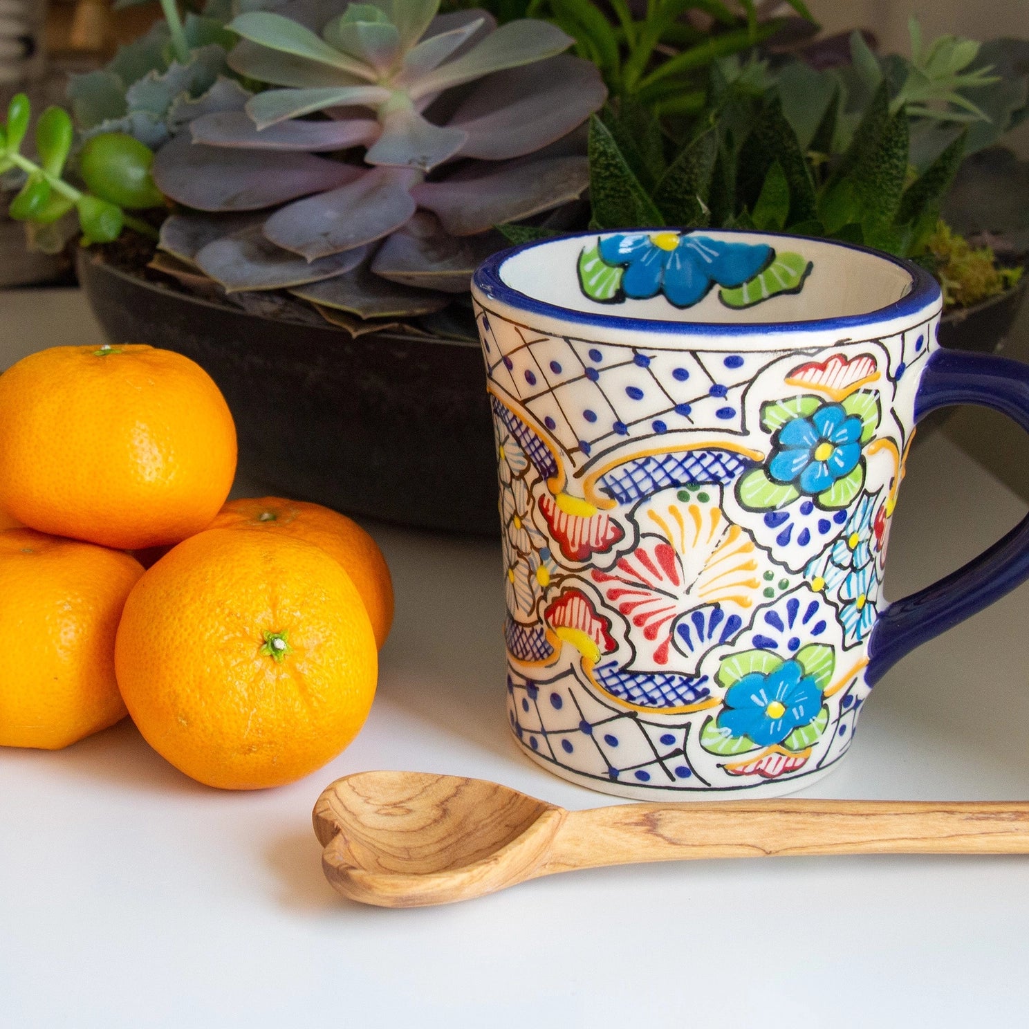 Hand-carved olive wood heart spoon shown with coffee cup and tangerines for size comparison