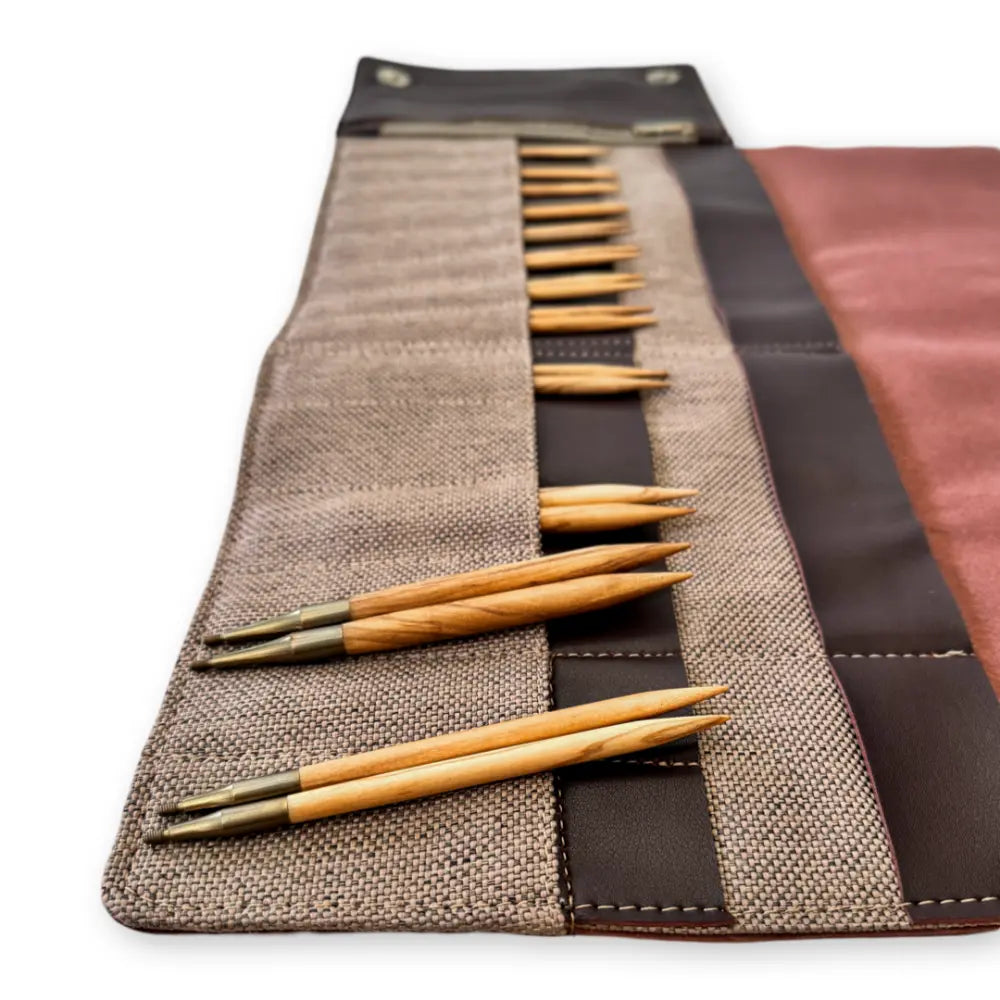 Set of wooden knitting needles in a brown fabric case on a white background