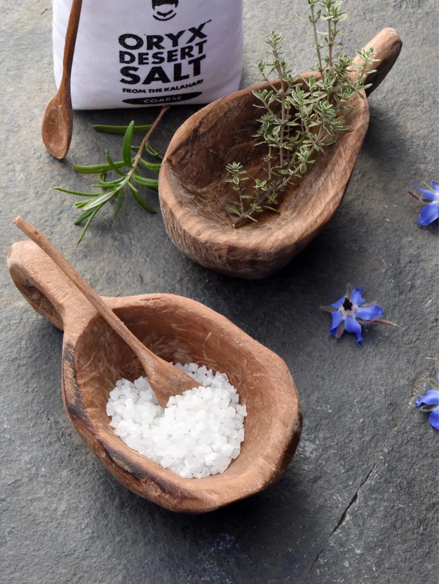 Wooden olive wood bowls with Salt and herbs on a dark surface