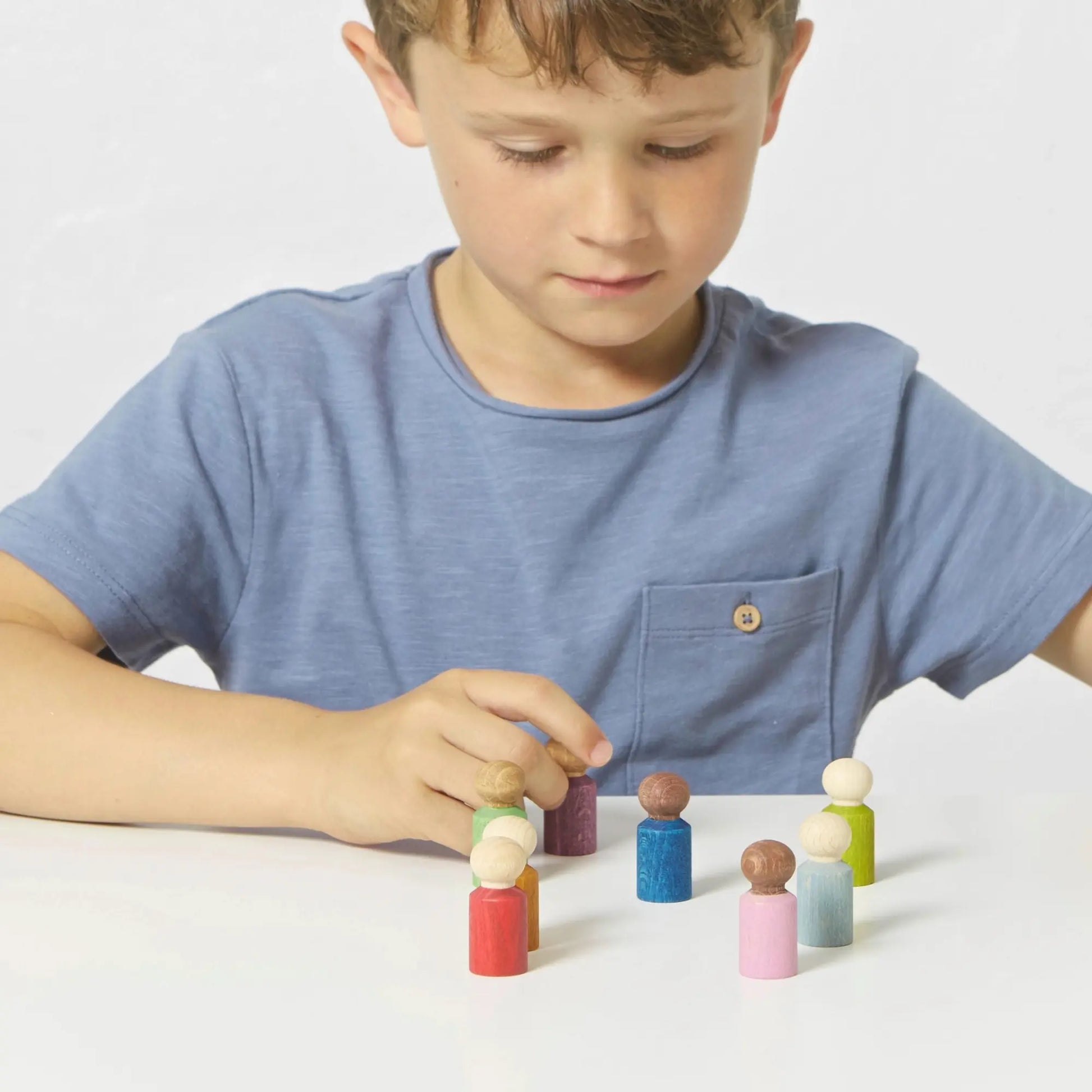 Child playing with Lubulona Lubu People wooden figures on a table, encouraging imaginative and open-ended play