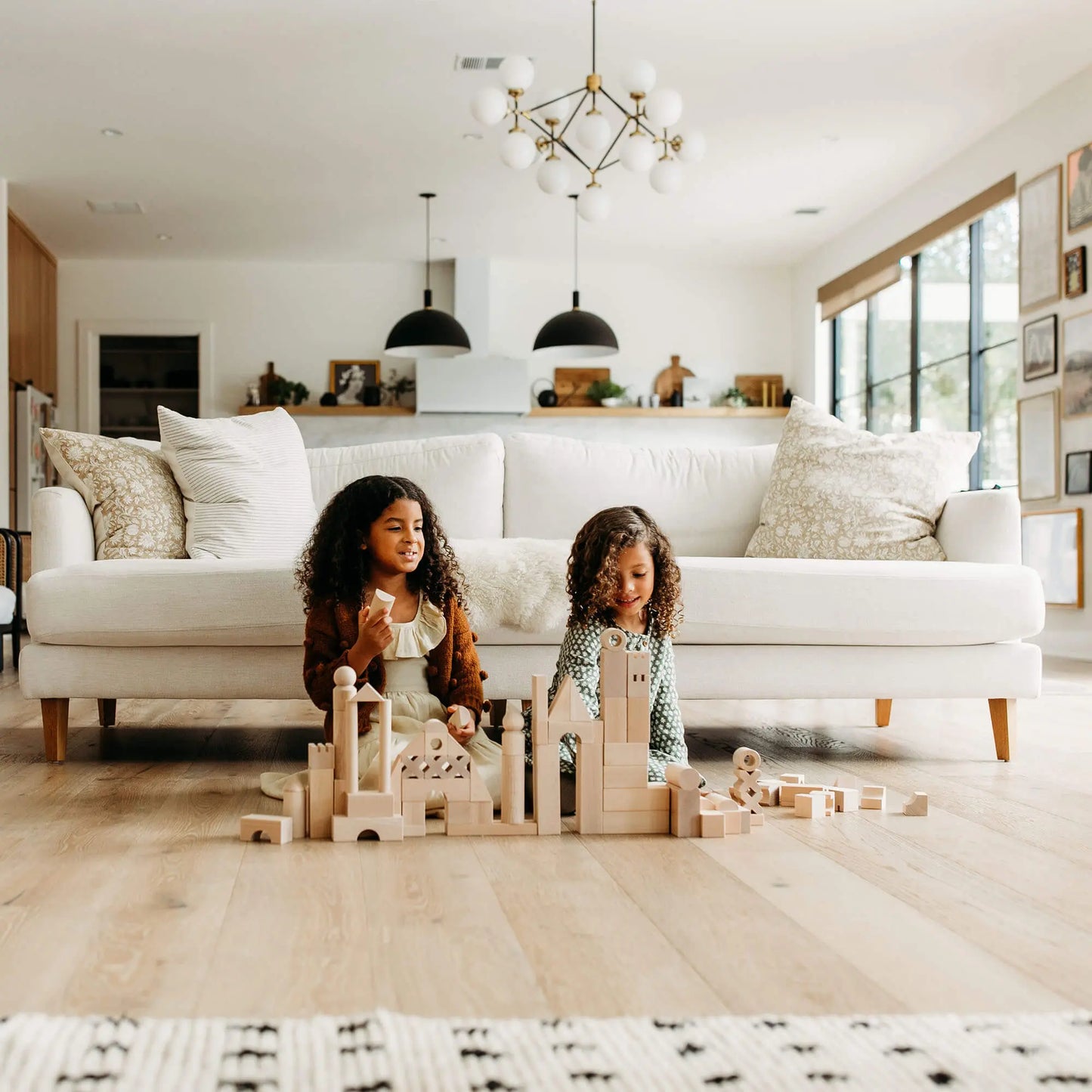 Two children playing with unpainted, natural wooden blocks in a modern living room.