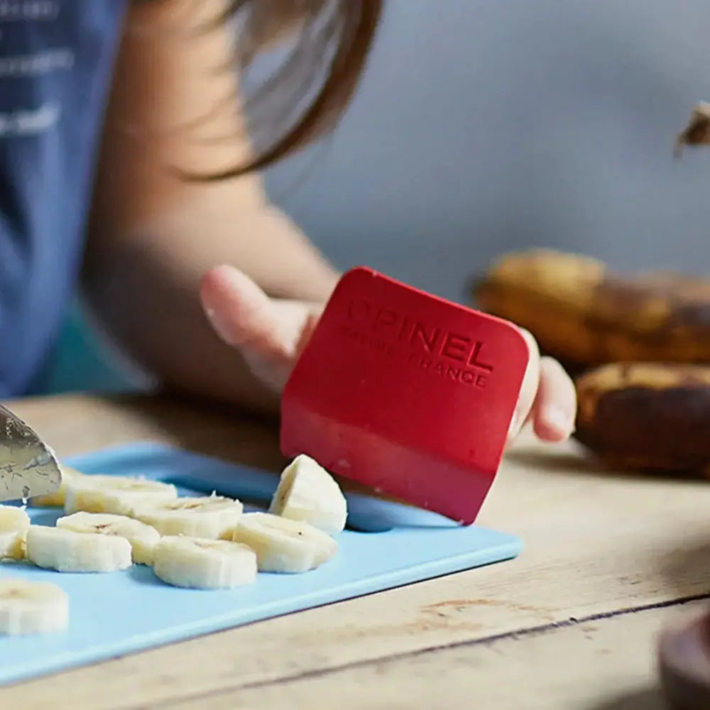 Opinel knife guard being used to cut bananas on a blue cutting board with a child's hand visible.