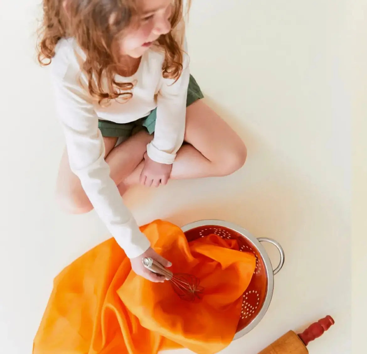 Girl stirring an orange playsilk in a pot with a wisk