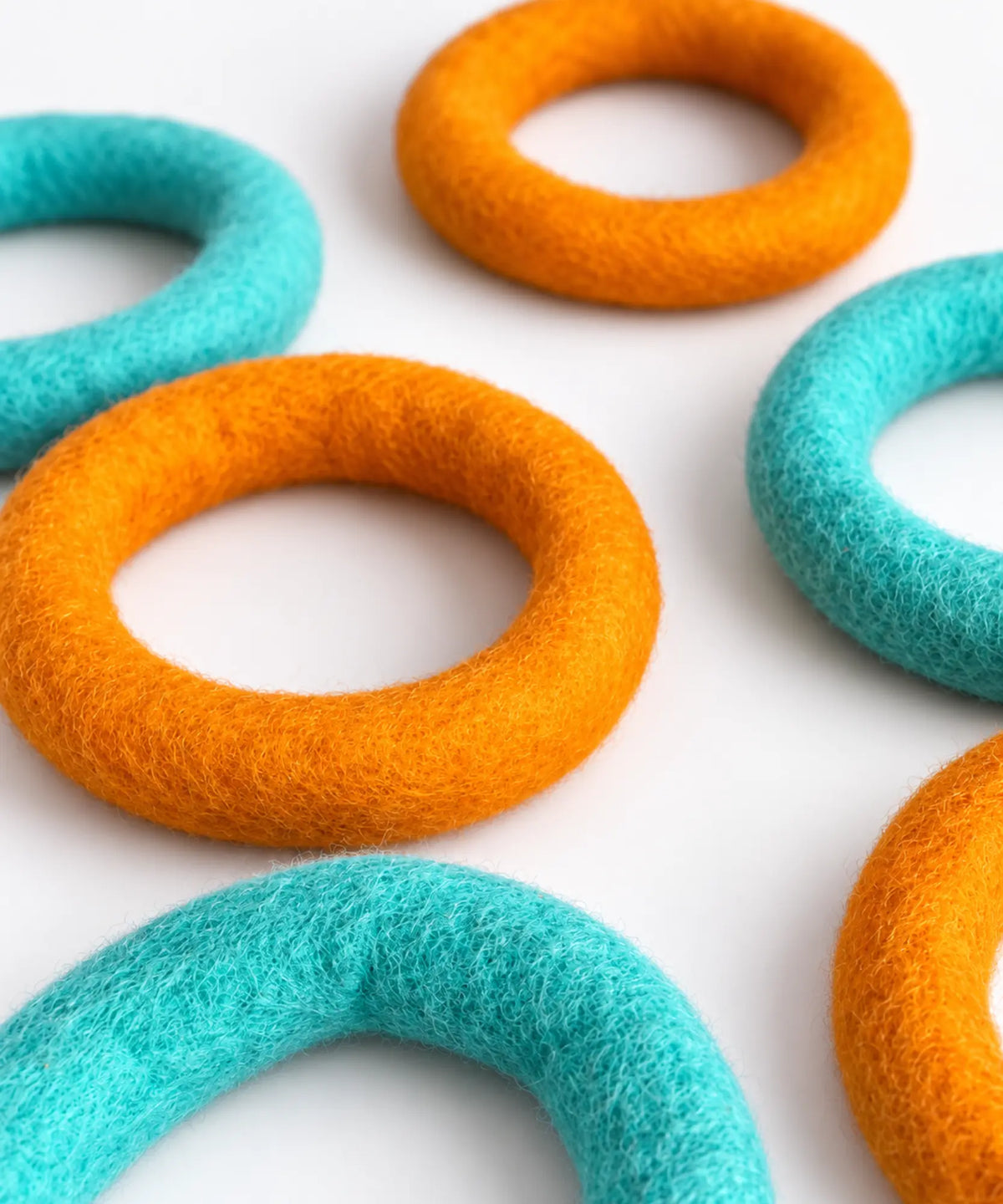Orange and teal wool felt rings laid flat in a scattered pattern on a white table.