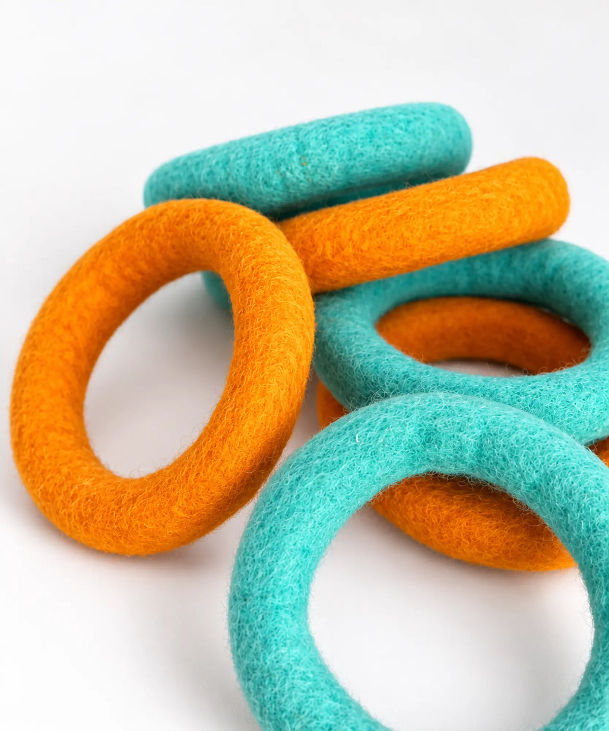 Orange and teal wool felt rings laid flat in a scattered pattern on a white table.